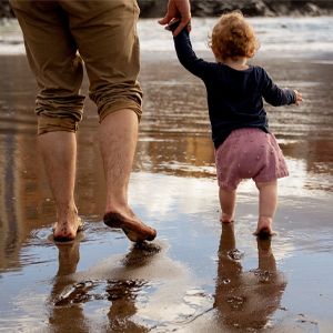 man walking on beach and holding hands with a toddler